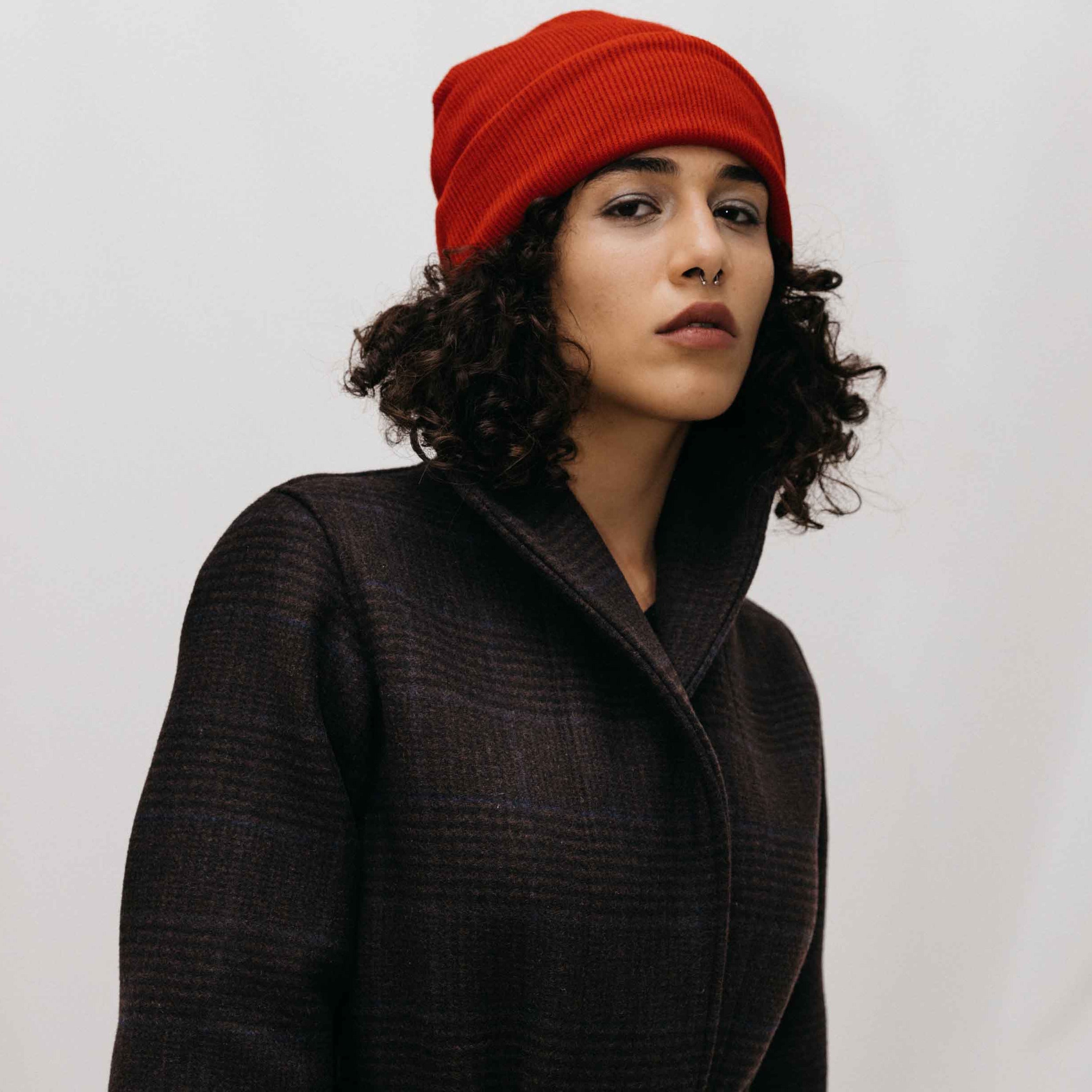 A person wearing a red ribbed beanie and a long black coat.