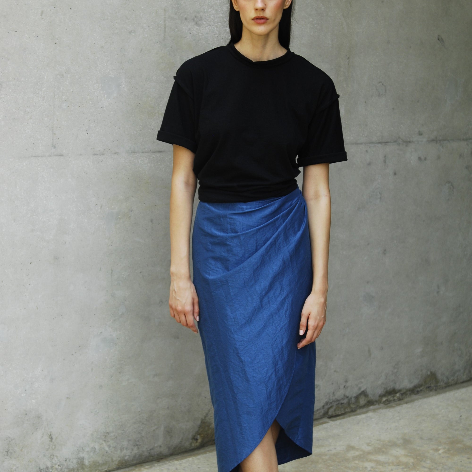 Woman wearing a relaxed fit black sana t-shirt and a blue skirt with an asymmetrical hem.