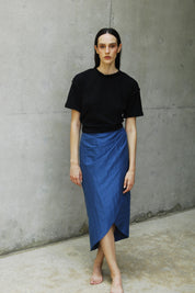 Woman wearing a relaxed fit black sana t-shirt and a blue skirt with an asymmetrical hem.