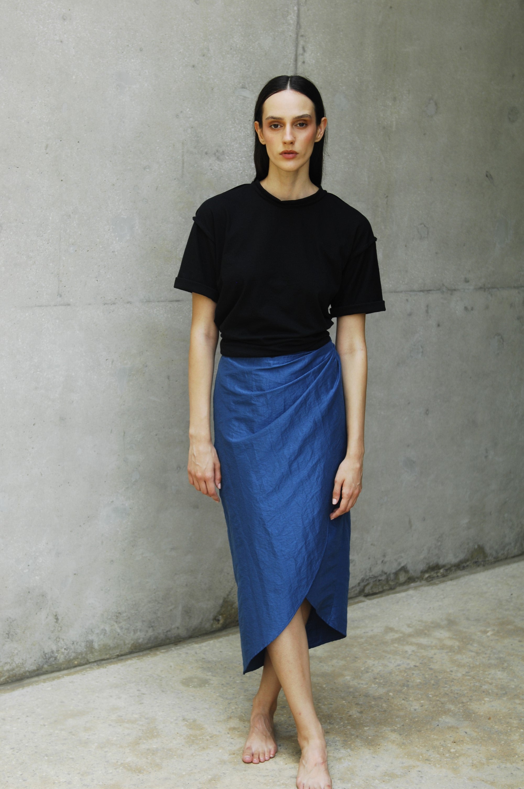 Woman wearing a relaxed fit black sana t-shirt and a blue skirt with an asymmetrical hem.