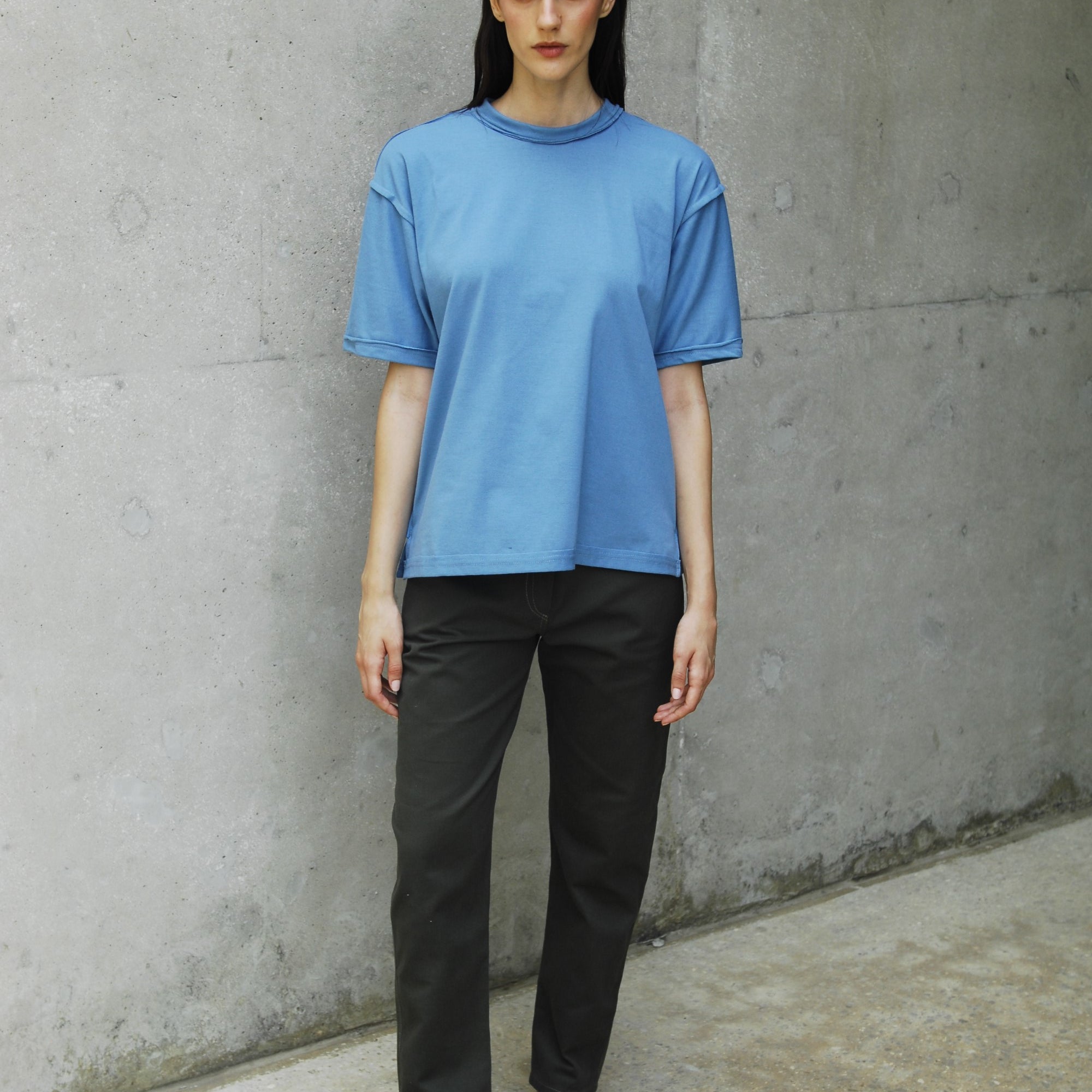 Woman wearing a relaxed fit blue t-shirt with long short sleeves and a sailor's neckline, paired with black pants.