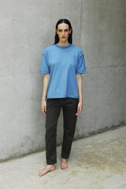 Woman wearing a relaxed fit blue t-shirt with long short sleeves and a sailor's neckline, paired with black pants.