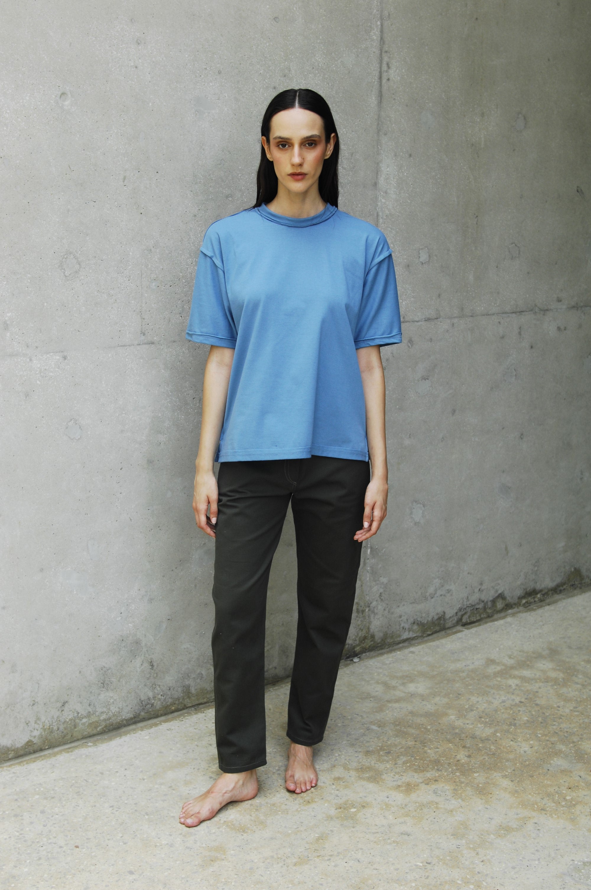 Woman wearing a relaxed fit blue t-shirt with long short sleeves and a sailor's neckline, paired with black pants.