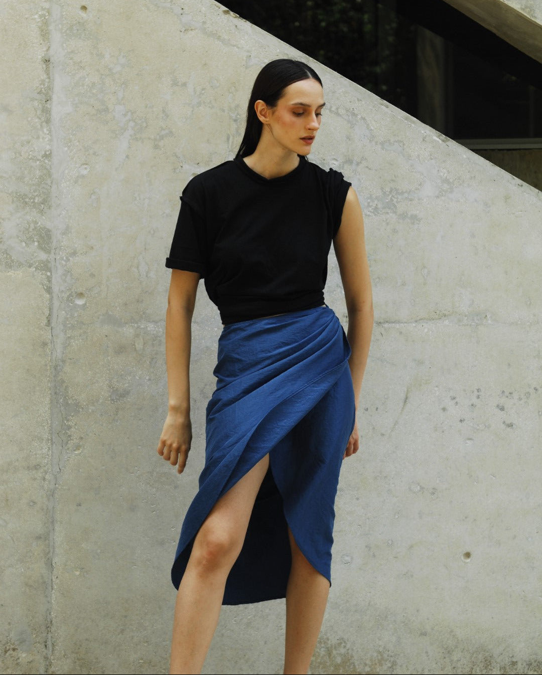Person in black top and blue skirt lying on a concrete surface