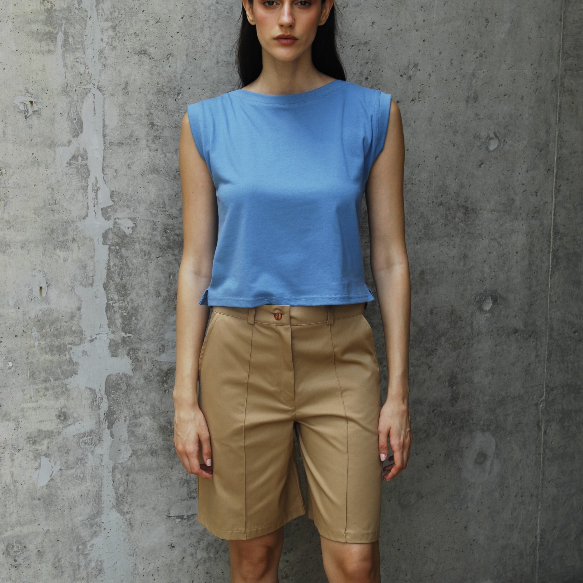 A woman standing wearing a Dahlia blue I-shirt with Camel shorts 