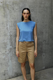 A woman standing wearing a Dahlia blue I-shirt with Camel shorts 