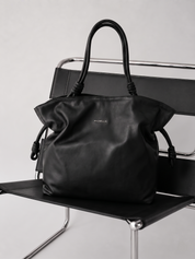 Black handbag with 'Michella' branding on a black chair against a light gray background