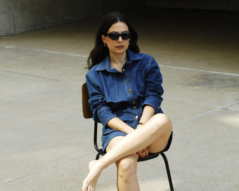 founder sitting on a chair in an outdoor setting wearing sunglasses and a denim outfit.