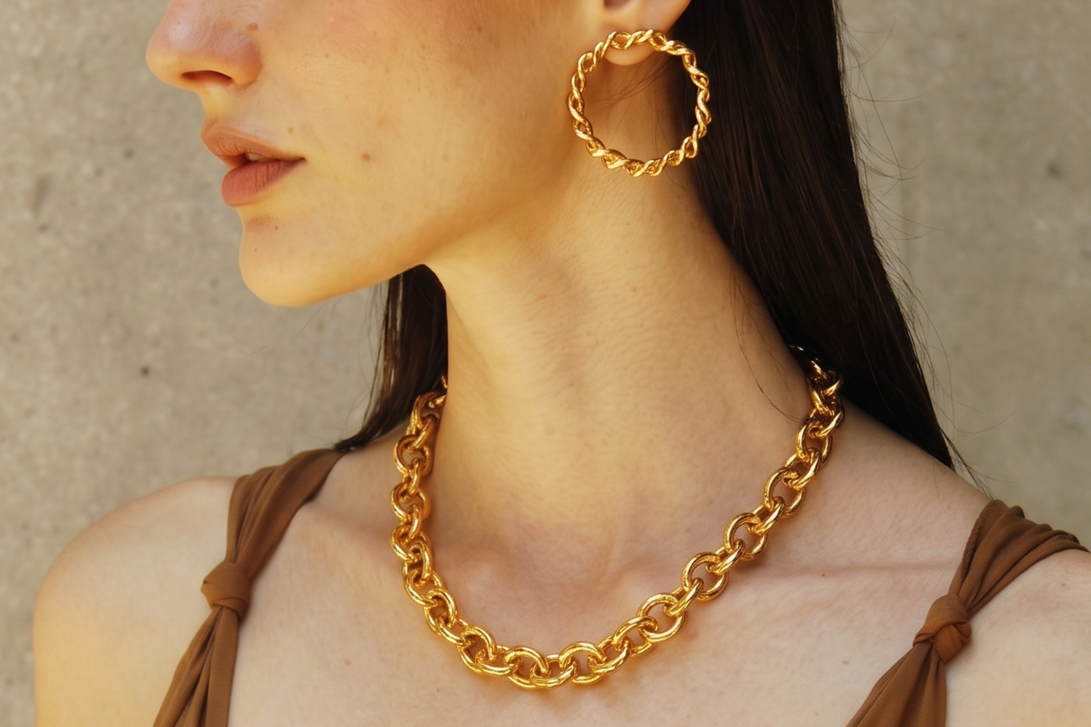 Woman wearing Sia gold hoop earrings and chain necklace against a beige wall