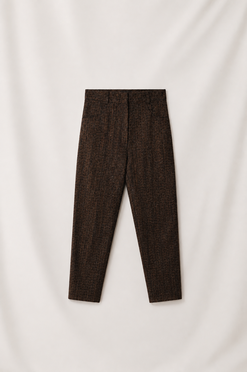 Dark brown textured tweed trousers laid flat against a draped off-white fabric background.