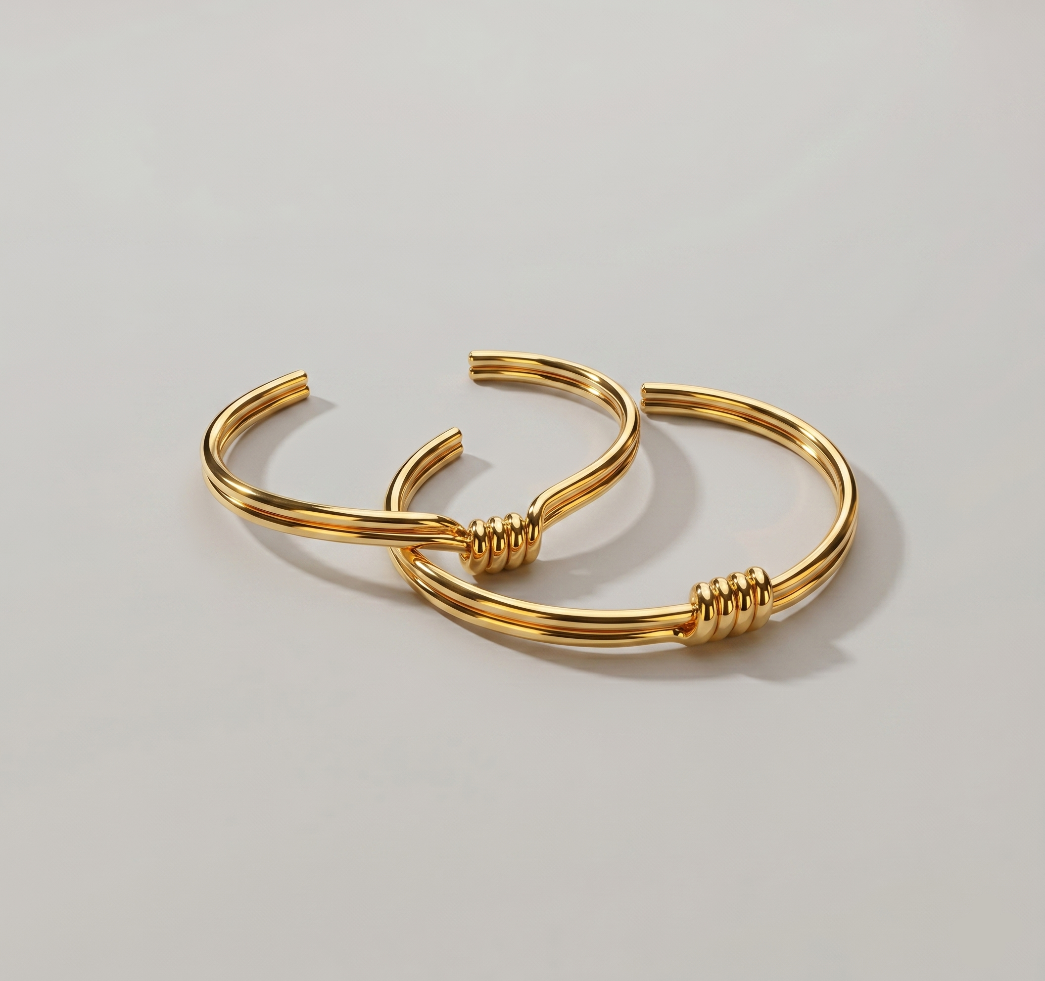 Pair of gold knot bracelets on a light gray background