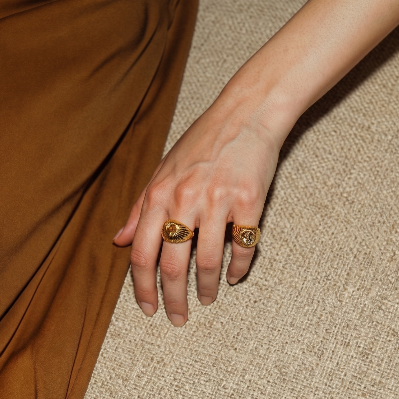 Hand wearing two gold rings on a textured surface
