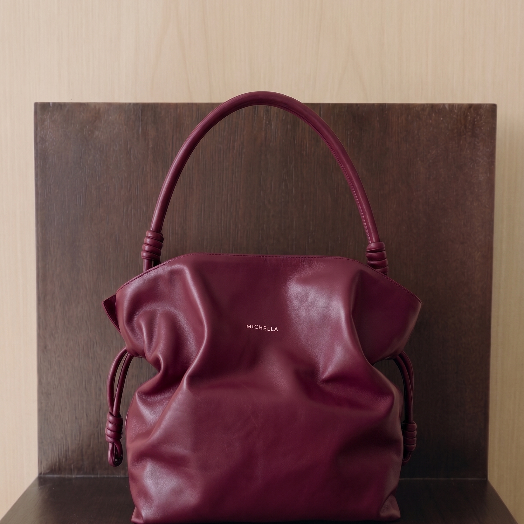 Maroon handbag with 'Michella' branding on a wooden surface.