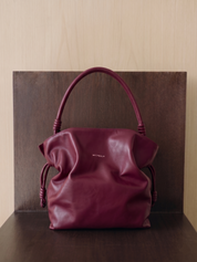 Maroon handbag with 'Michella' branding on a wooden surface.