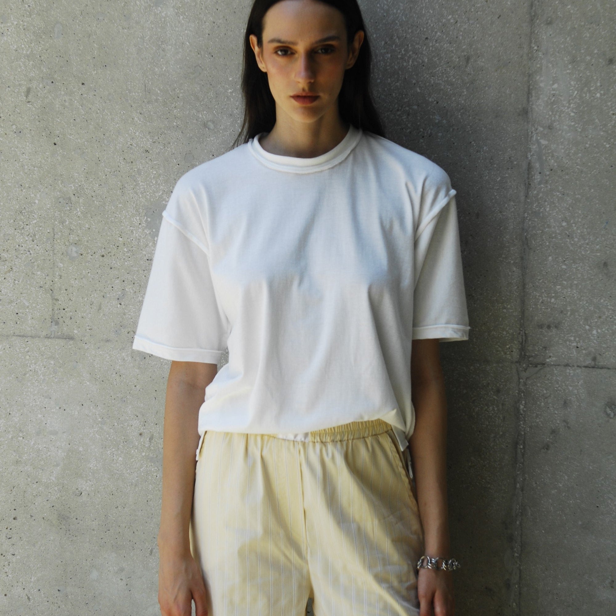 Person wearing sana white t-shirt and light-colored pants against a concrete wall.