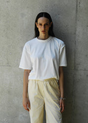 Person wearing sana white t-shirt and light-colored pants against a concrete wall.