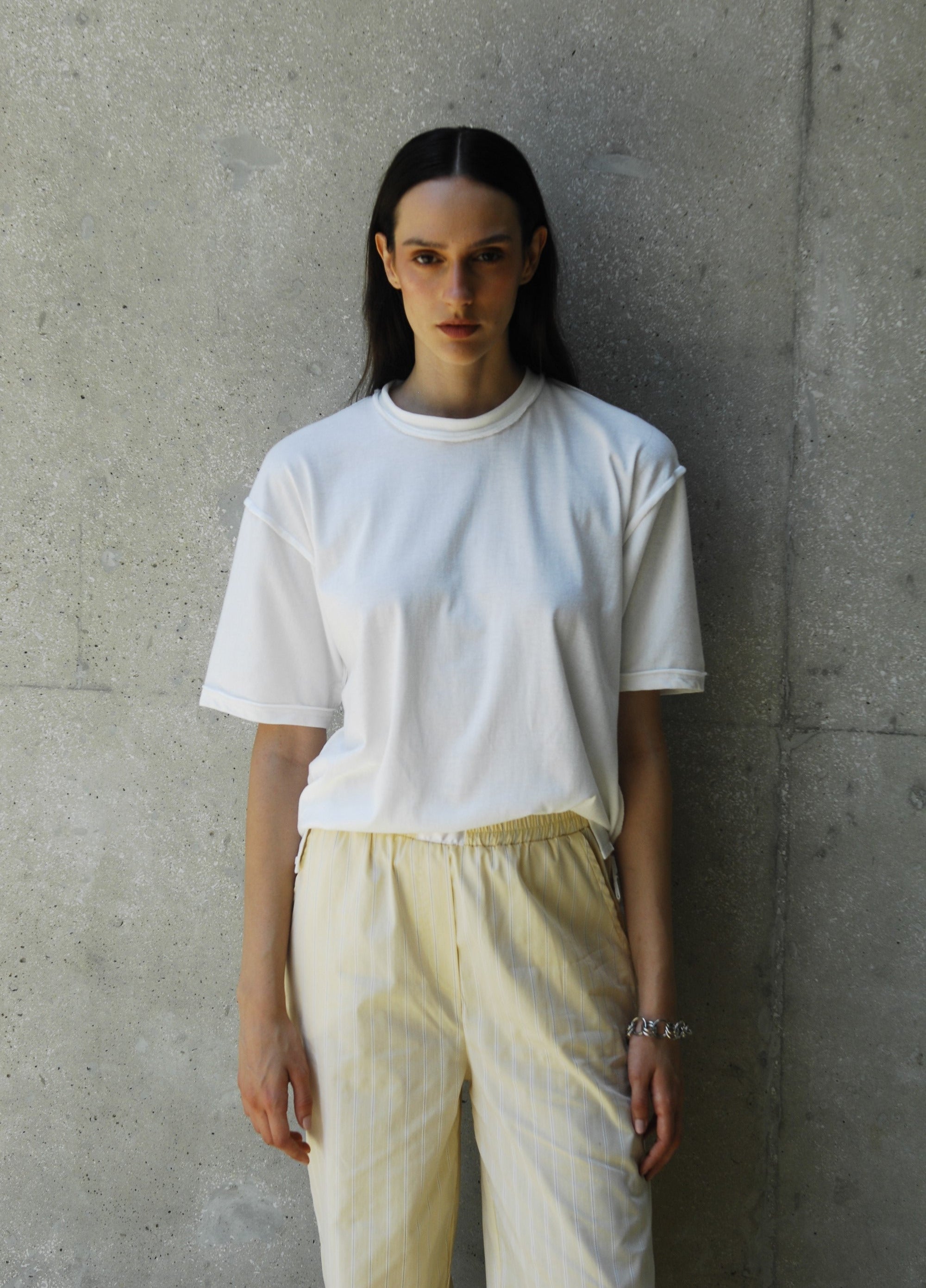 Person wearing sana white t-shirt and light-colored pants against a concrete wall.