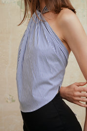 A high-necked halter top with button closure, featuring a striped pattern in blue and white. The top is designed with an open back and waist ties.