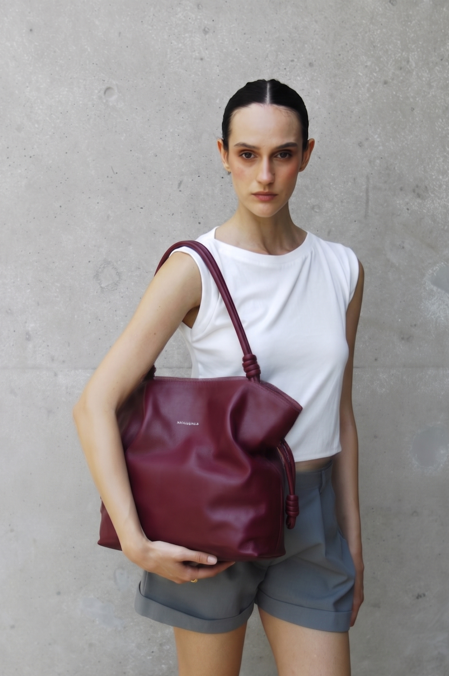 Woman holding Rumi burgundy handbag against a gray concrete wall