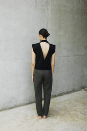 woman wearing a black backless vest and khaki pants standing on a concrete floor.