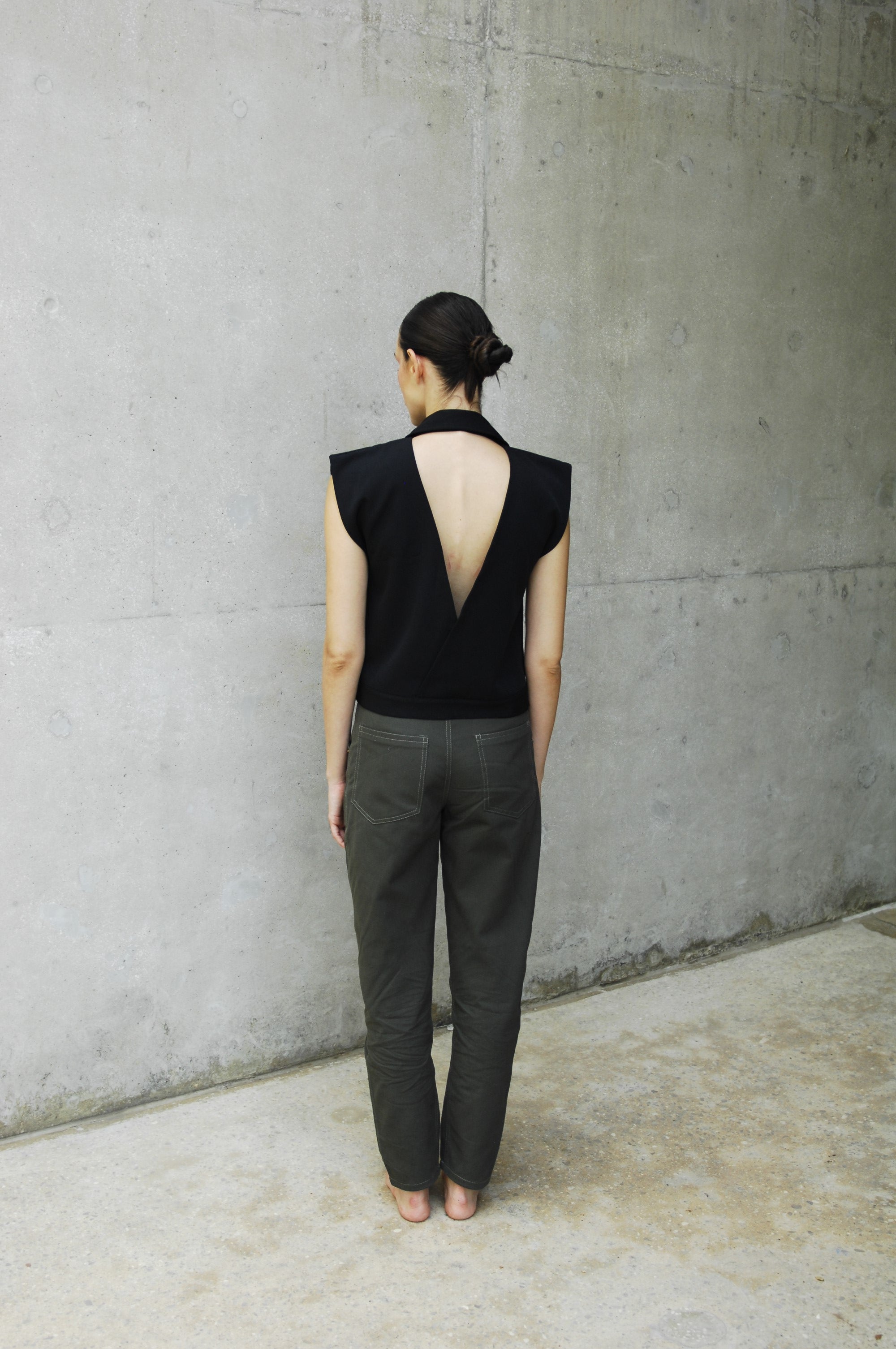 woman wearing a black backless vest and khaki pants standing on a concrete floor.