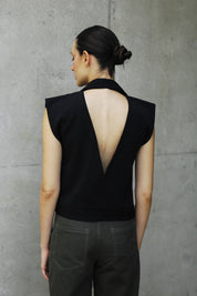 woman wearing a black backless vest and dark pants on a gray concrete floor.