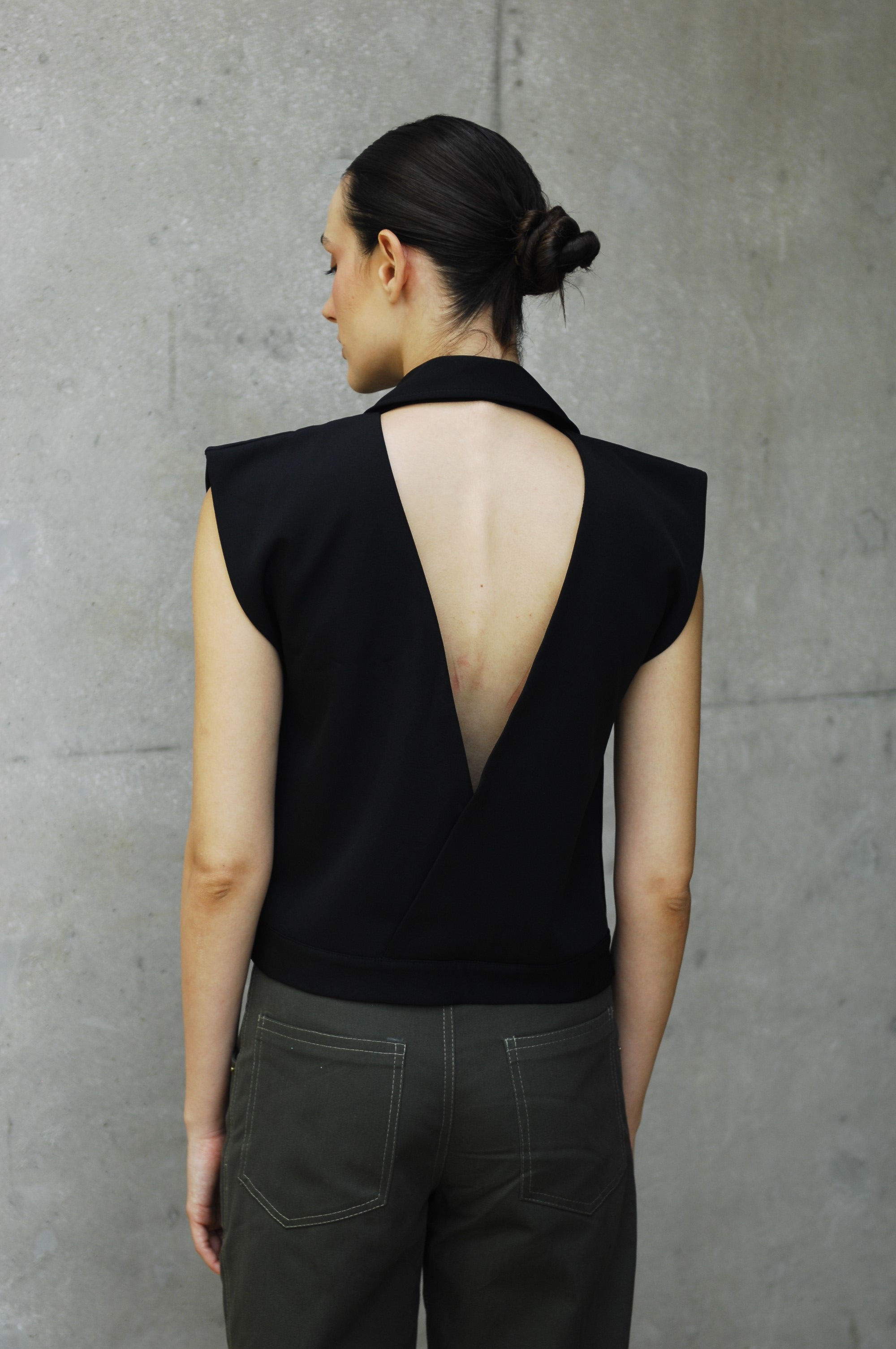 woman wearing a black backless vest and dark pants on a gray concrete floor.
