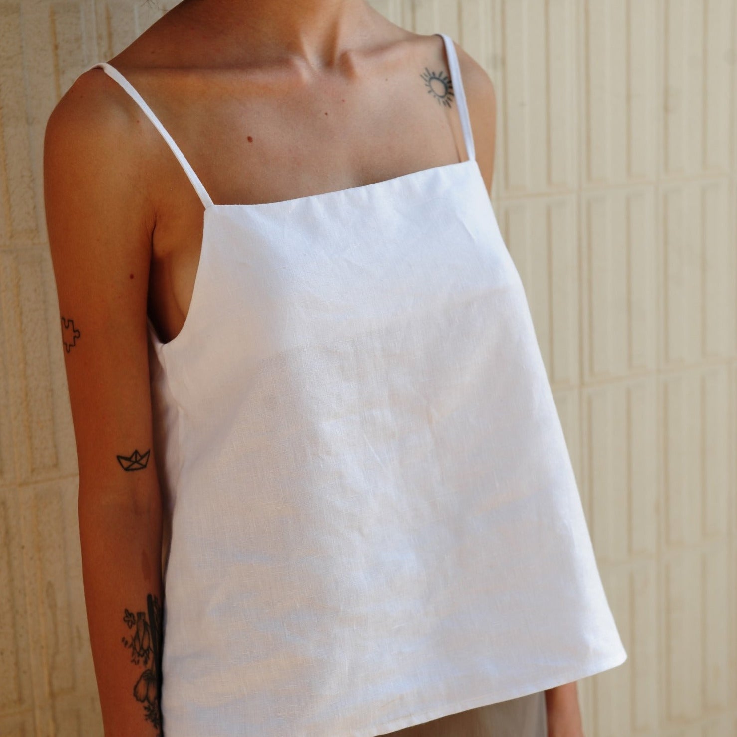 model wearing a white Lea Linen Camisole with spaghetti straps and a square neckline.