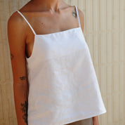 model wearing a white Lea Linen Camisole with spaghetti straps and a square neckline.