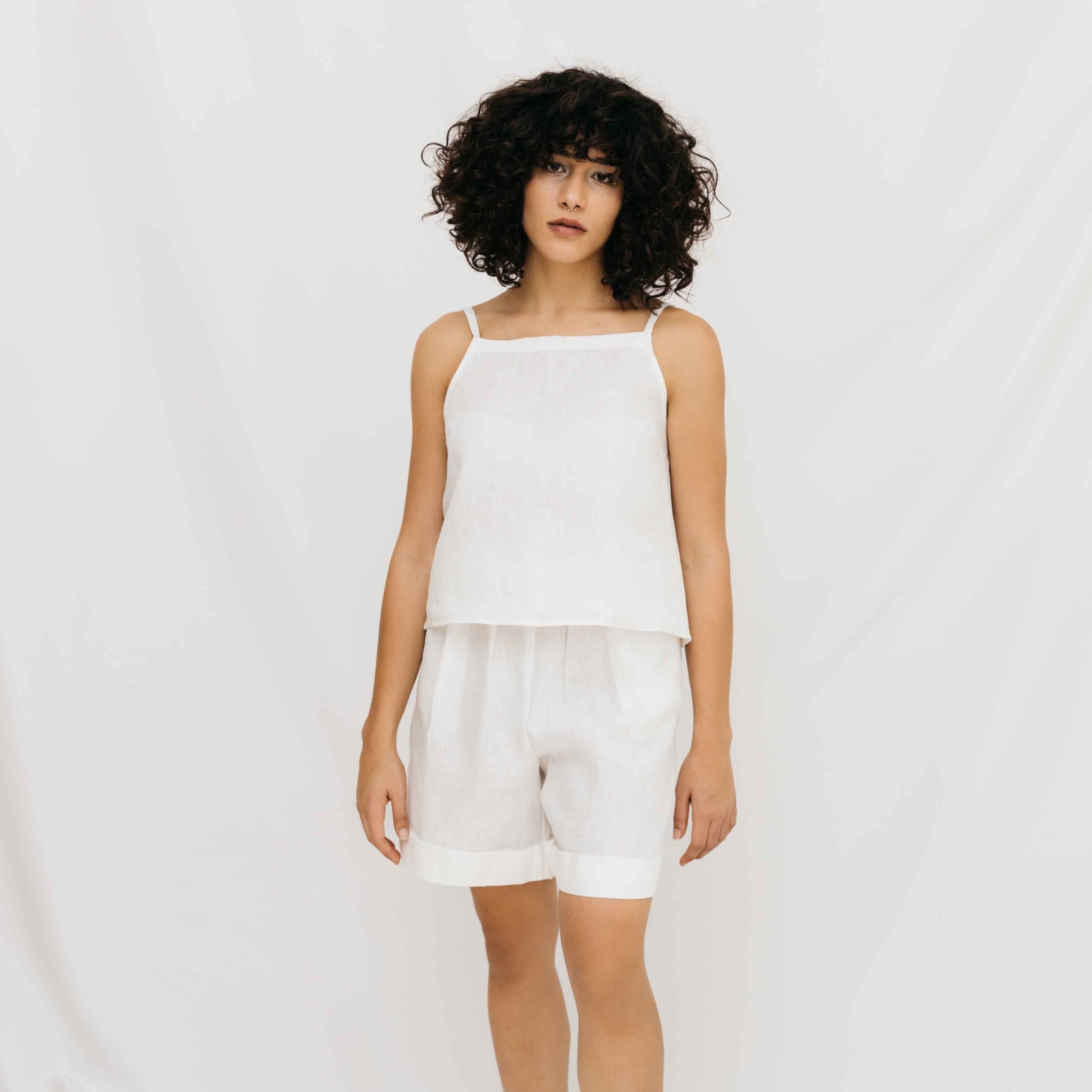 A model wearing high-waisted white linen shorts and a matching top, standing against a white background.